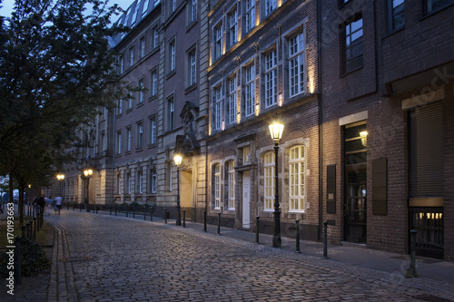 Evening view of old, historical buildings and cobblestone street in Altstadt Dusseldorf. People walk in blurry motion.