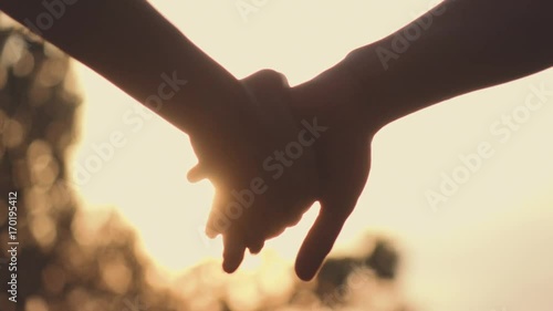 Close up of two Lovers Joining Hands. SLOW MOTION 240 fps. Detail Silhouette of Man and Woman holding hands over the Sunset Lake Background. Couple Trust, Love and Happiness concept. 