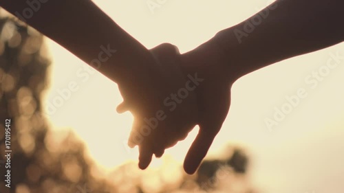 Close up of two Lovers Joining Hands. SLOW MOTION 240 fps. Detail Silhouette of Man and Woman holding hands over the Sunset Lake Background. Couple Trust, Love and Happiness concept.  photo