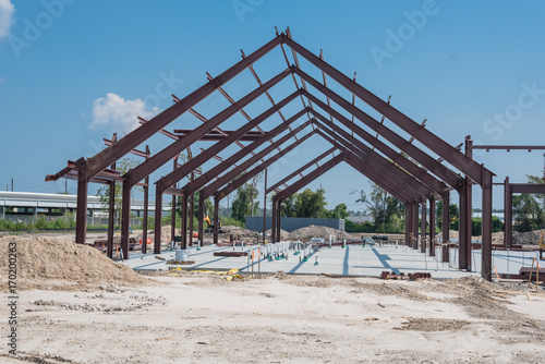 Steel structure of new industrial building under cloud blue sky. New technology structural frame beam of factory in construction. Steel frame manufacturer and pile of sand and gravel in Crosby, TX, US