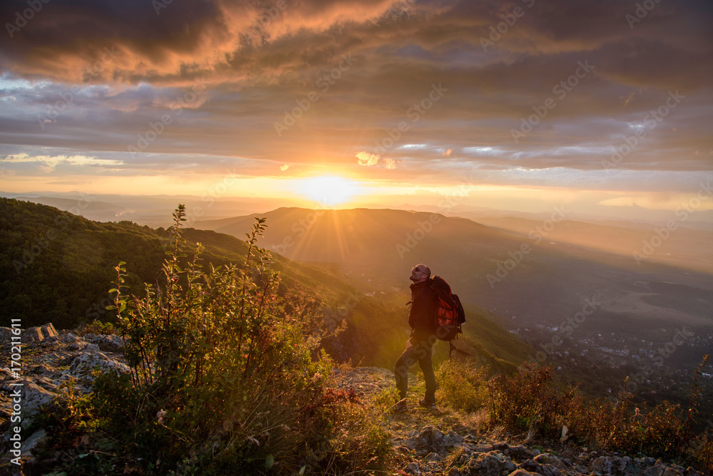 Amazing sunset on a mountain top - man with alpine equipment enjoying the breathtaking view under the stormy sky