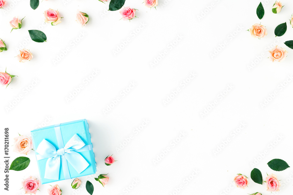 Frame of blue gift box and pink roses flat lay