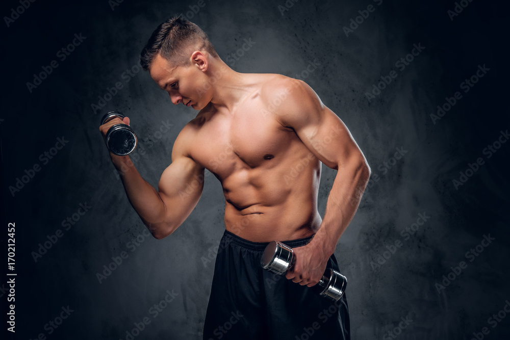 Shirtless male holds a set of dumbbells.