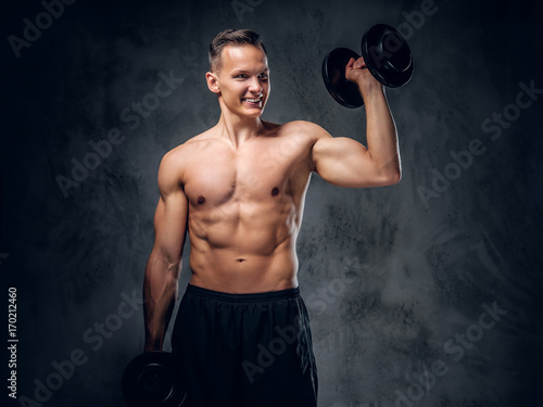 Shirtless male holds a set of dumbbells.