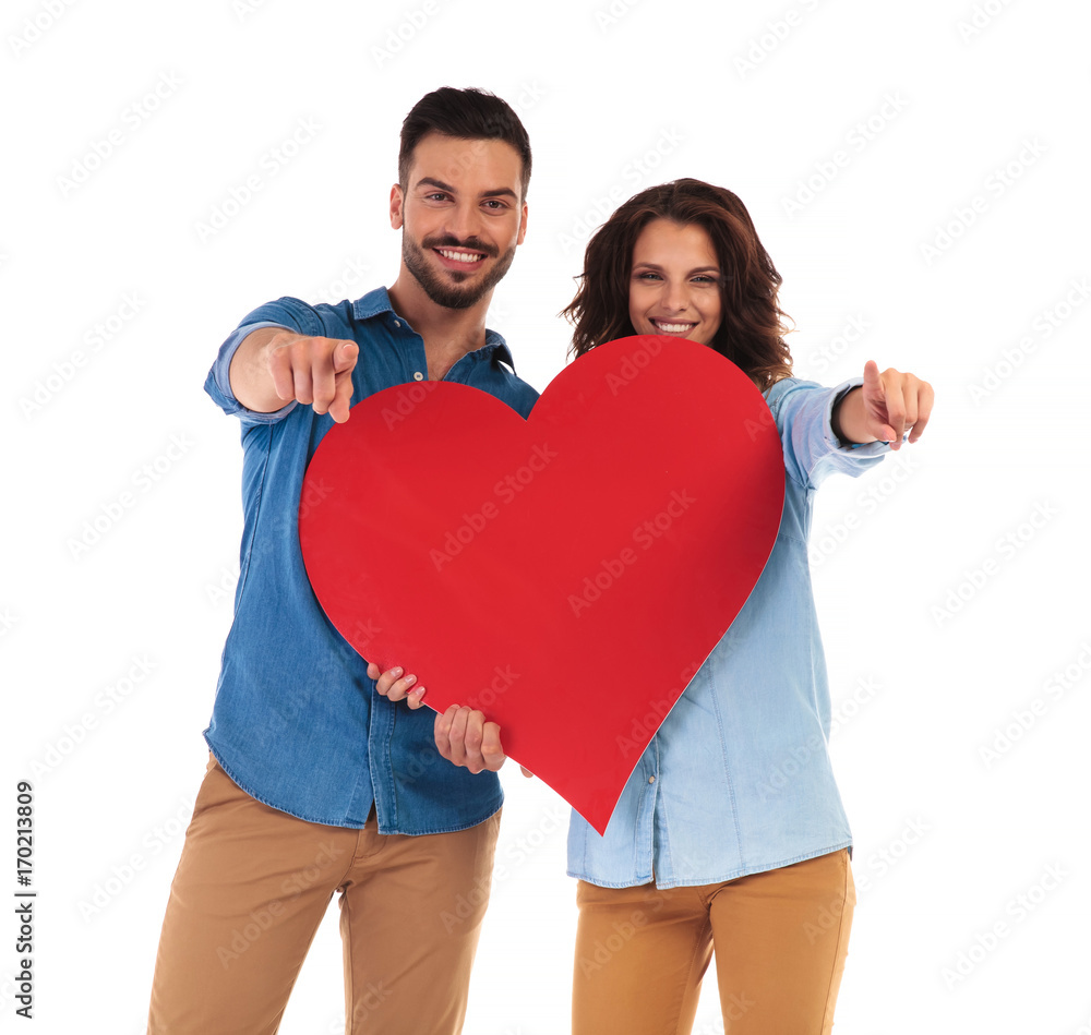happy casual couple holding big heart and pointing fingers