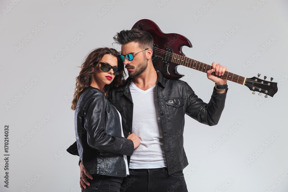 Fototapeta premium cool punk man holding guitar on shoulder and embracing woman