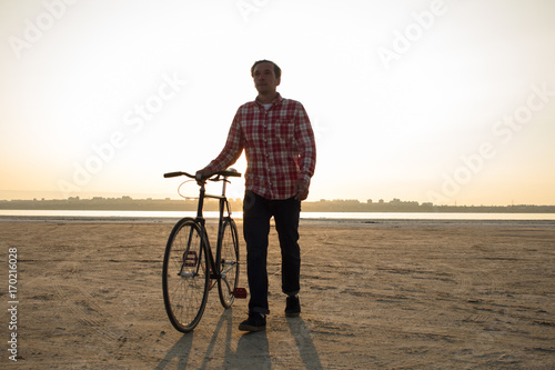 bicycle rider walking with retro black bike during sunrise at the desert 