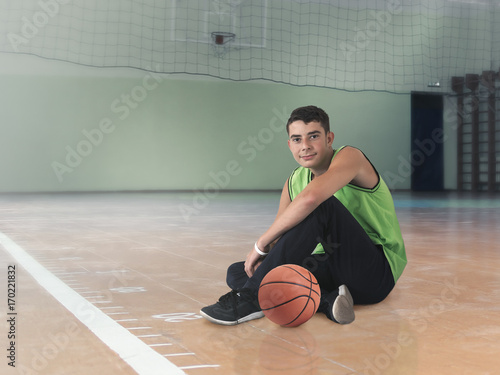 The student is sitting on the floor in the gym with the basketball © kozorog