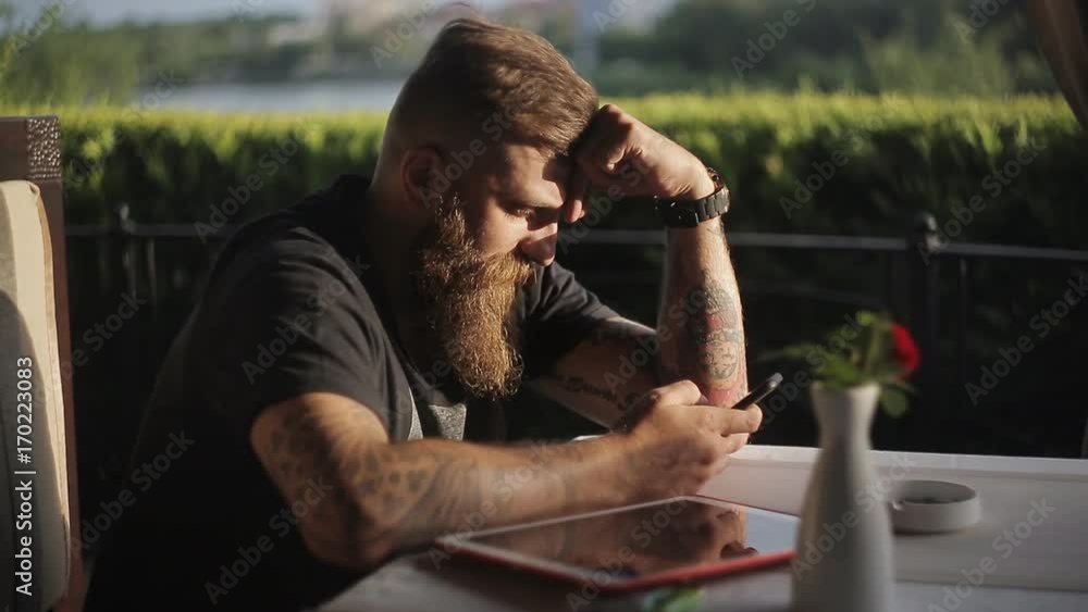 Man sitting at cafeteria or restaurant holding smart phone, looking at its screen. Man using gadget. Man sitting at cafeteria or restaurant holding smart phone, looking at its screen. Man using gadget.