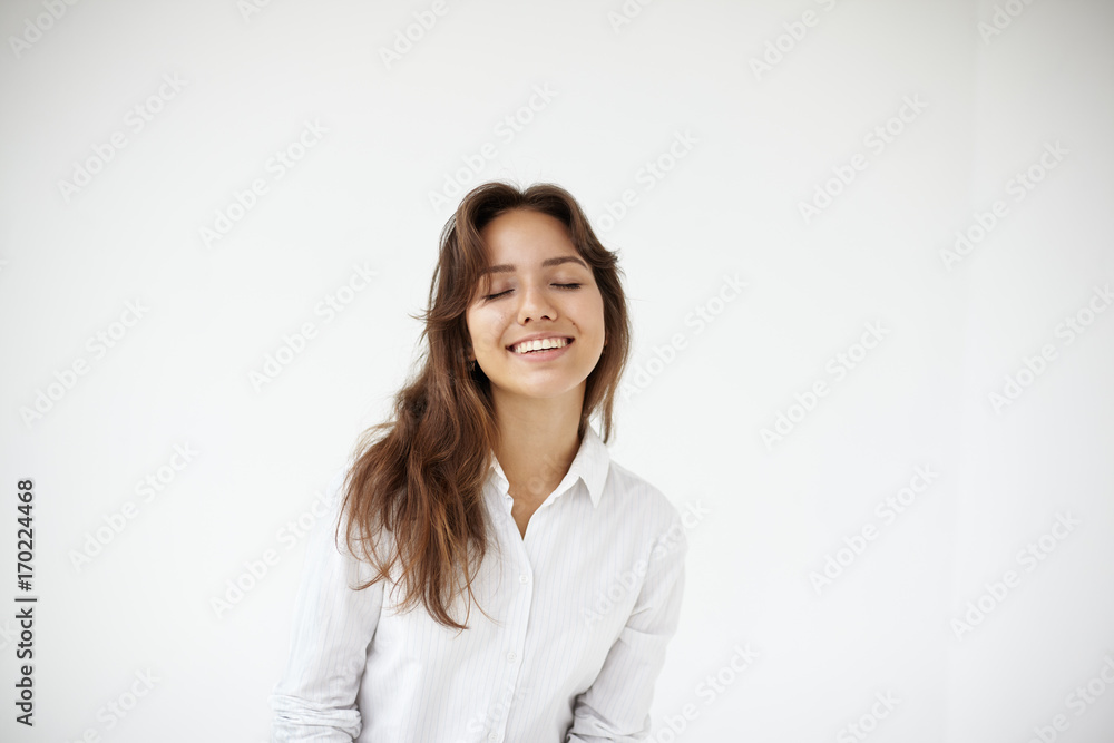 Portrait of happy joyful young woman office worker in formal blouse posing isolated at white wall with eyes closed in great pleasure and delight. Genuine positive emotions, happiness and joy Portrait of happy joyful young woman office worker in formal blouse posing isolated at white wall with eyes closed in great pleasure and delight. Genuine positive emotions, happiness and joy