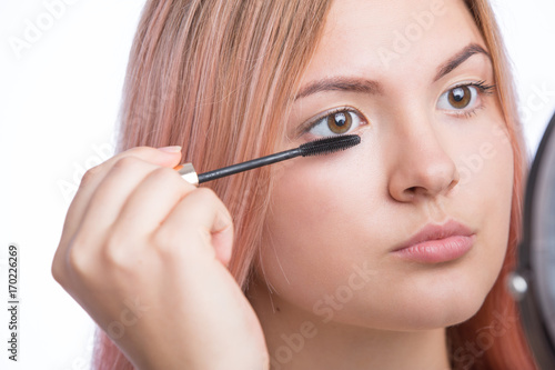 Portrait of a beautiful young woman applying mascara on eyelashes