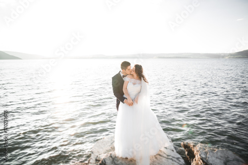 Wedding couple kissing and hugging on rocks near blue sea © olegparylyak