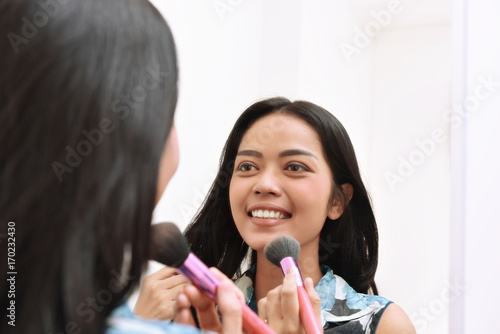 Beautiful asian girl applying makeup while looking on the mirror