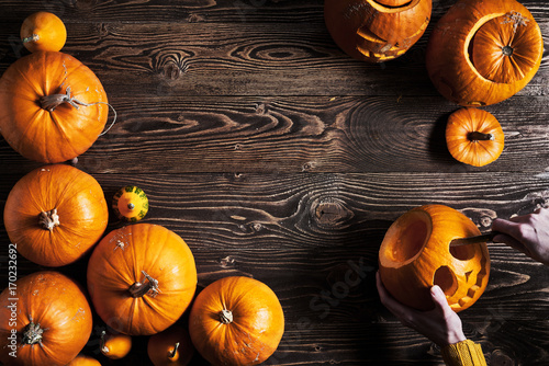 Картината върху платно Hands carving jack-o-latern from pumpkin over wooden background, top view, flat