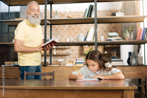 Fototapeta Joyful grandfather dictating words to his granddaughter