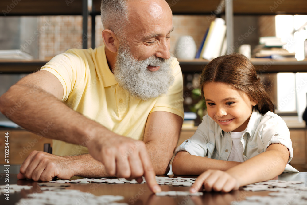 Adorable little girl assembling jigsaw puzzle with her grandfather Adorable little girl assembling jigsaw puzzle with her grandfather