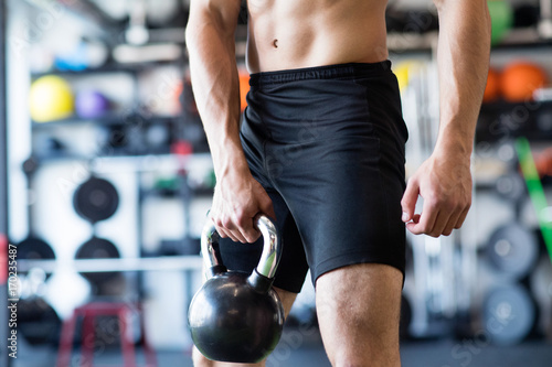 Unrecognizable young fit man in gym exercising with kettlebell.