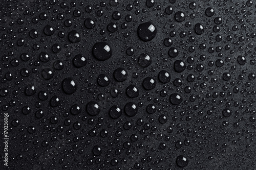 Water drops on black grainy surface, dark background