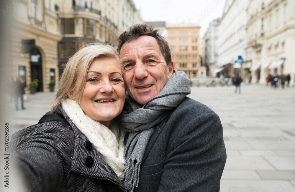 Beautiful senior couple on a walk in city centre taking selfie.