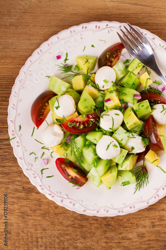 Avocado salad with tomato, cucumber and mozzarella. Cheese and vegetable salad. View from above, top studio shot