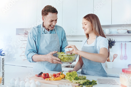 Radiant father and female child making salad together photo