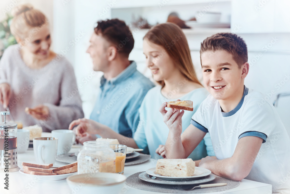 Happy youngster smiling into camera while having breakfast with family