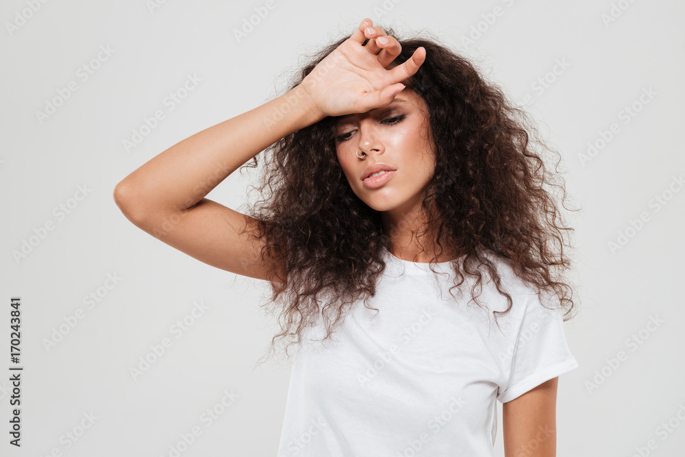 Tired curly woman with closed eyes holding hand on forehead Tired curly woman with closed eyes holding hand on forehead