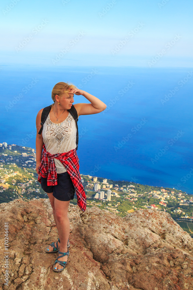 Girl with a backpack standing on top of a mountain.