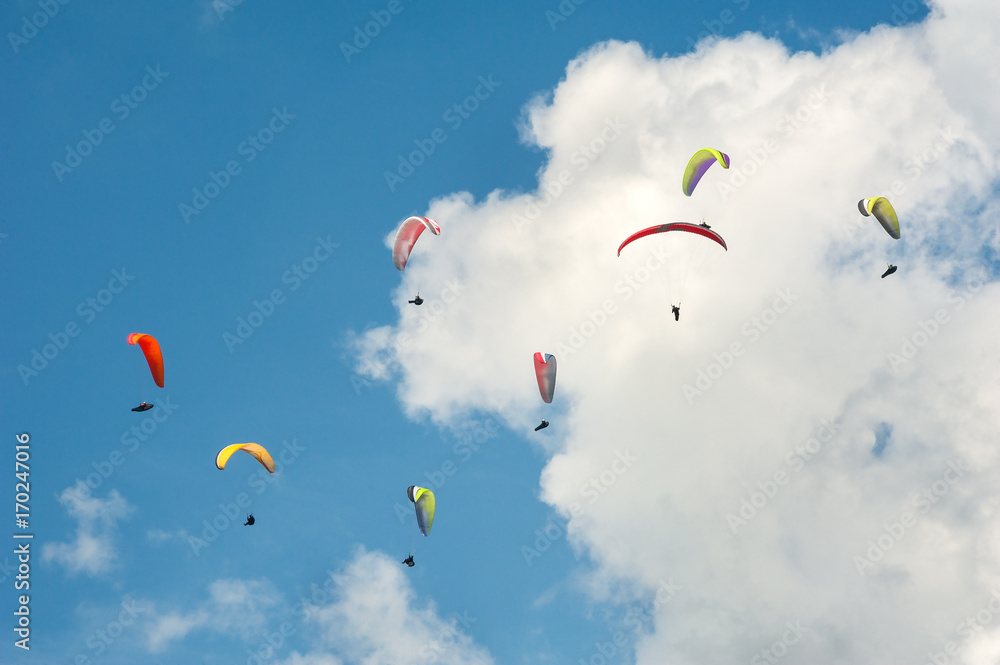 Paragliding in the blue sunny sky. Group of paragliders fly in summer sunny day. Carpathians, Ukraine. Paragliders against the background of clouds. Paragliding in the blue sunny sky. Group of paragliders fly in summer sunny day. Carpathians, Ukraine. Paragliders against the background of clouds.