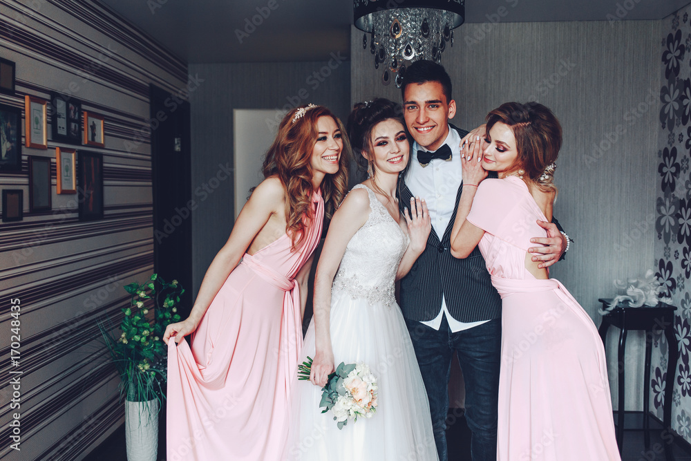 Stylish wedding at home. Young cute newlyweds hug along with bridesmaids at home..Cheerful young newlyweds along with cute bridesmaids Stylish wedding at home. Young cute newlyweds hug along with bridesmaids at home..Cheerful young newlyweds along with cute bridesmaids