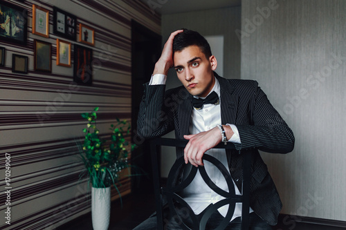 Принти на полотні A young cute suitor in a dark suit with a bow tie in his room