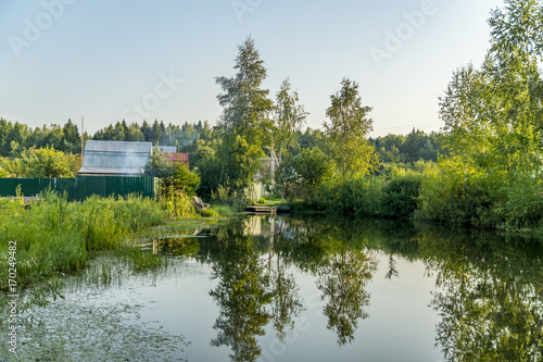 Wooden gottage near old pond and forest with reflection in water