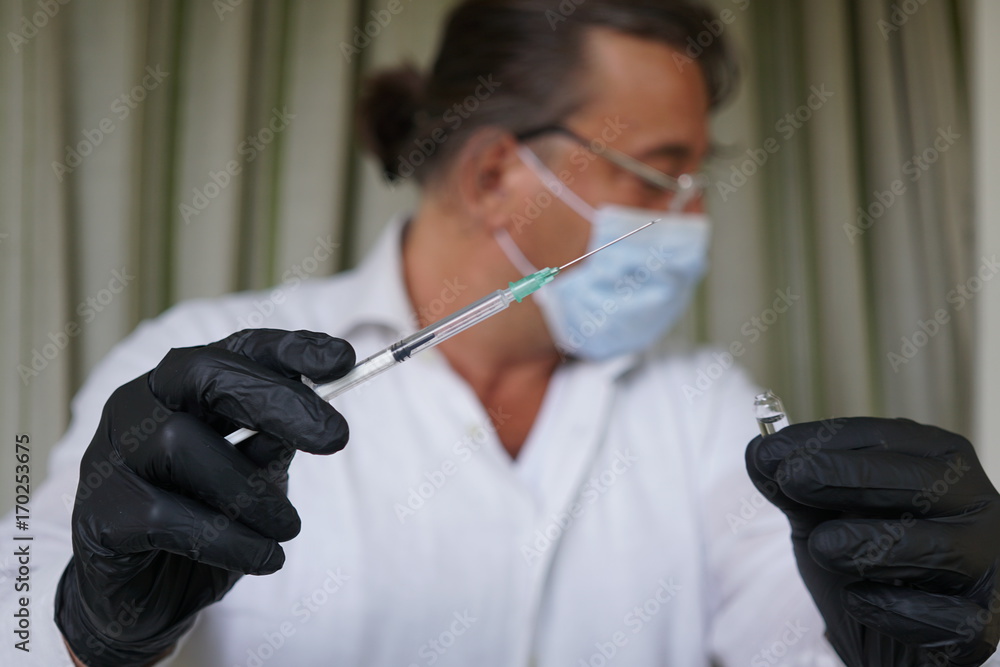 Male caucasian doctor wearing a flu mask and black gloves holding a syringe Male caucasian doctor wearing a flu mask and black gloves holding a syringe