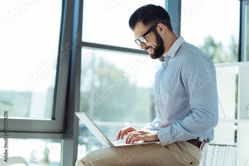 Smiling man typing on laptop while sitting on table