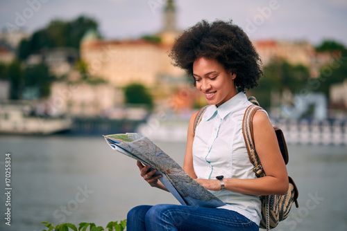 Mixed race tourist sitting on dock and planing tour through the city while looking at map