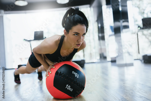 Sport, people and lifestyle concept. Active athletic woman doing intense core workout in gym. Strong female doing core exercise on fitness mat with weight medicine ball in health club.