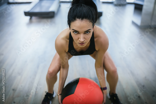 Close-up shot of fit female doing intense core workout in gym. Young muscular woman doing core exercise and squatting on fitness mat in health club with medecine ball. © iuricazac