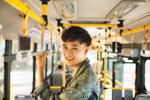 Asian man taking public transport, standing inside bus.