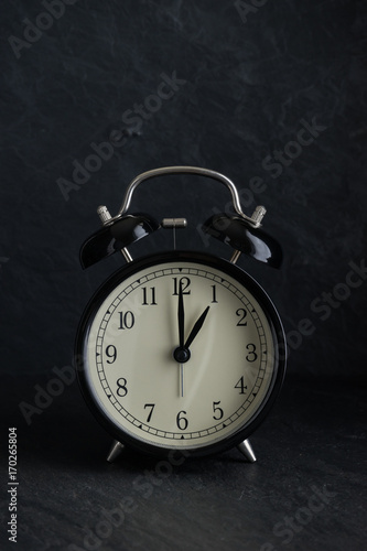 black alarm clock with stone background at one o'clock