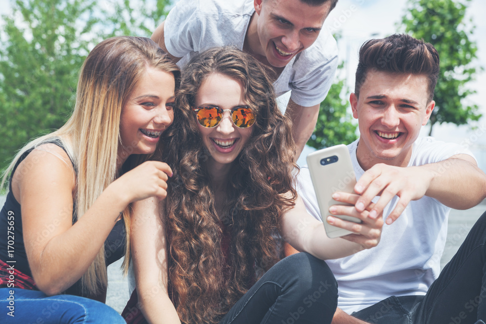 Fototapeta premium Group of friends sitting together using phone and laughing