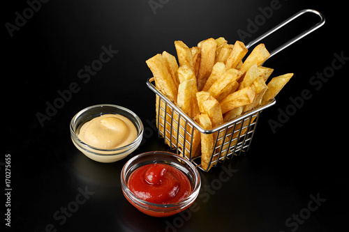 French fries in basket with ketchup and sauce isolated on black background. Above view.