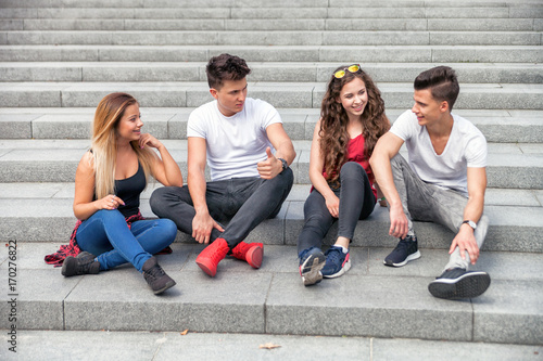 Group of friends sitting together on stairs and talking, city background