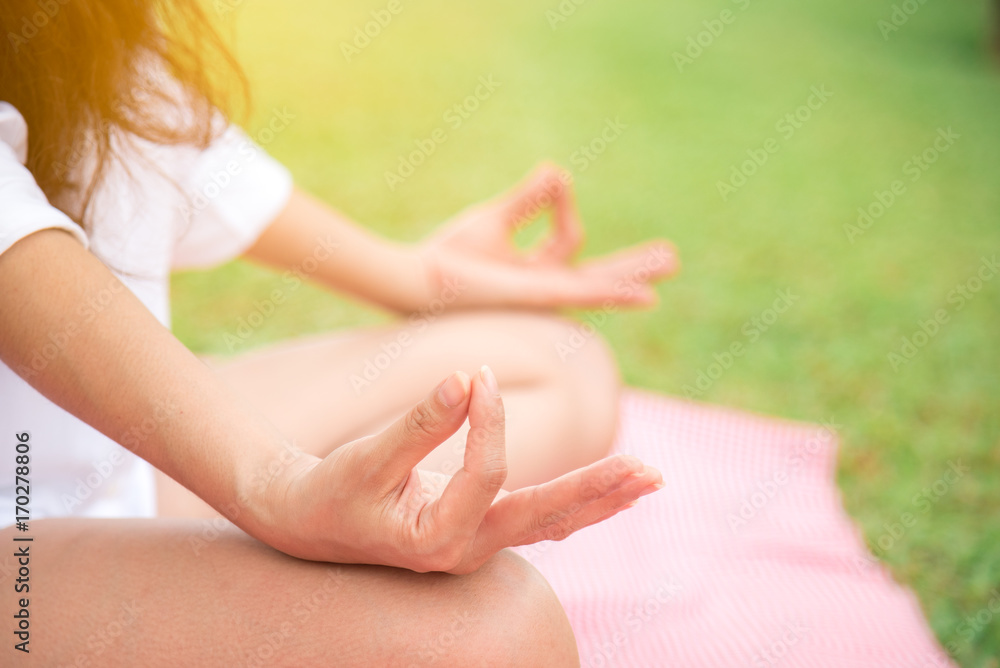 Naklejka premium Closeup side view of asian woman meditating in lotus yoga position with sunshine at park. Wellbeing and healthy lifestyle. Health concept.