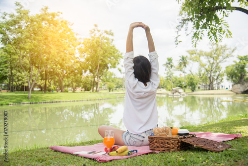Closeup of young woman streching and relaxing with fruit basket and glass of orange juice in the park at weekend. Wellness. Health and food concept.