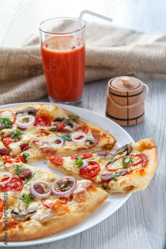 Sliced whole fresh pizza with tomatoes, salami, cheese and mushrooms on white plate