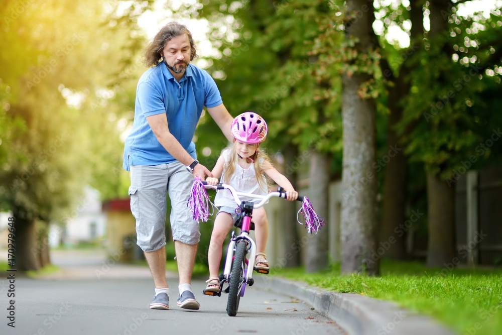 Happy father teaching his little daughter to ride a bicycle. Child learning to ride a bike.