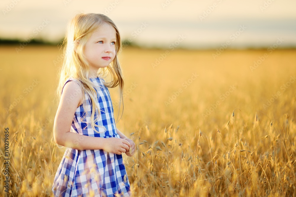 Adorable girl walking happily in wheat field on warm and sunny summer evening