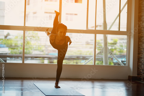 Asian woman doing yoga in a room with sunlight coming through the window.