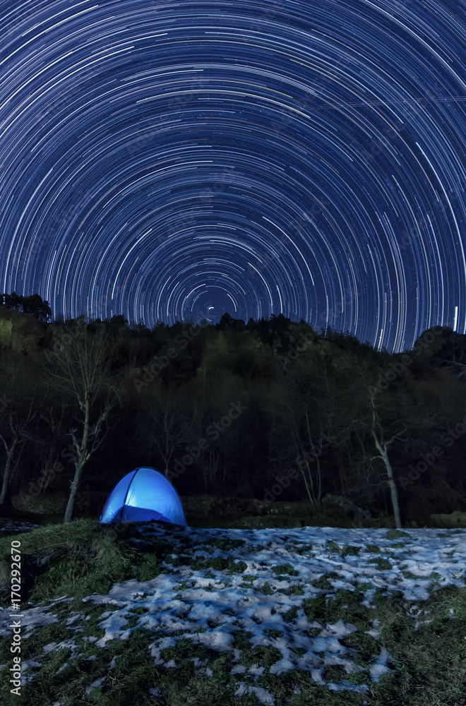 Fototapeta startrail with a illuminated tent on the foreground