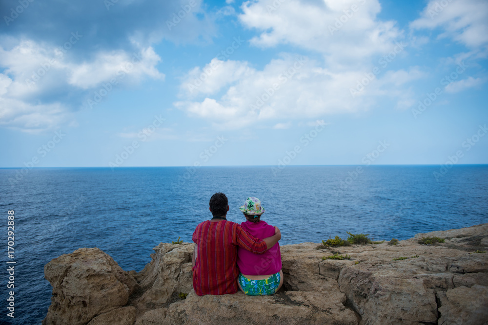 Romantic couple sitting on a cliff and admirig wonderful seascape